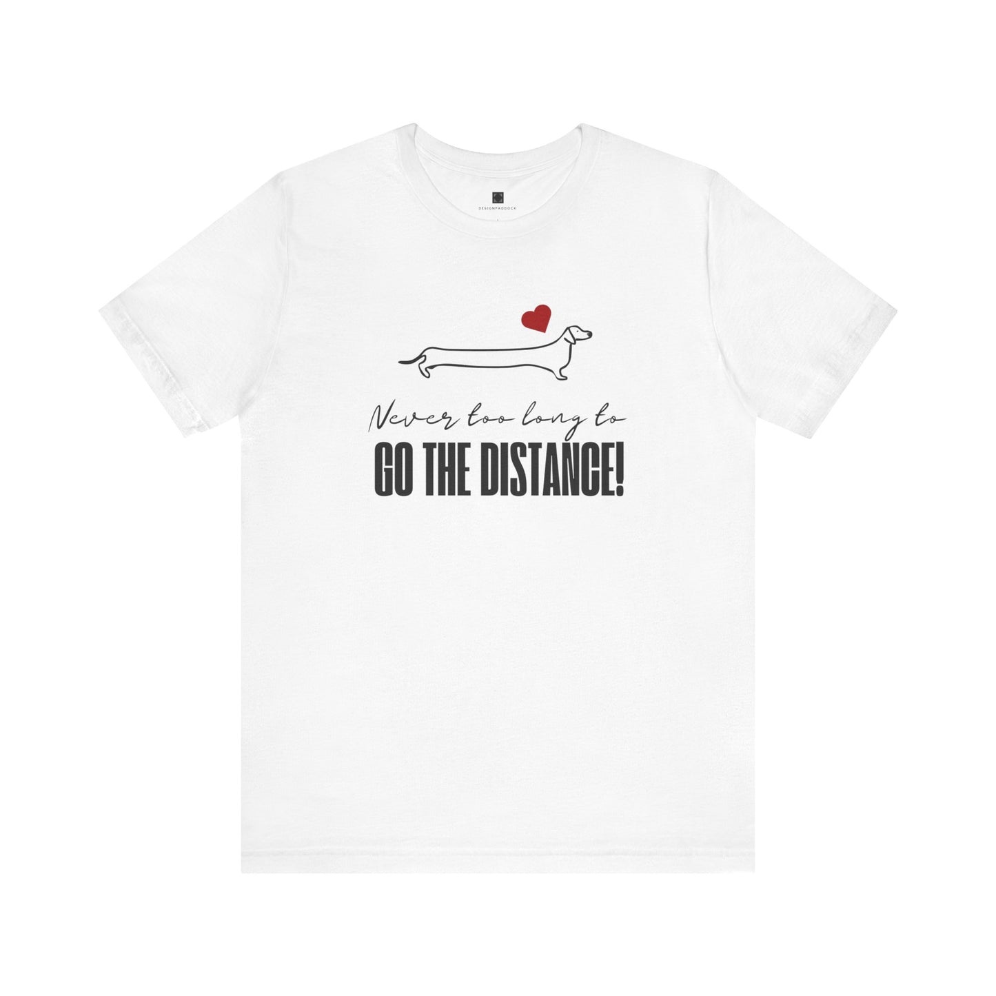 White Dachshund t-shirt laid flat on a white background, featuring a minimalist Dachshund design, red heart, and the phrase “Never too long to GO THE DISTANCE!”